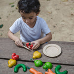 The PlanToys Wonky Fruit & Vegetables being played with by a child, the child is cutting the tomato in half using the wooden knife that is included. 