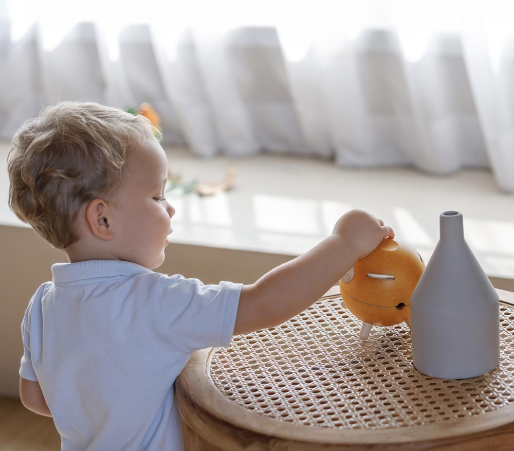 A child putting a coin in the PlanToys Yellow Piggy Bank.
