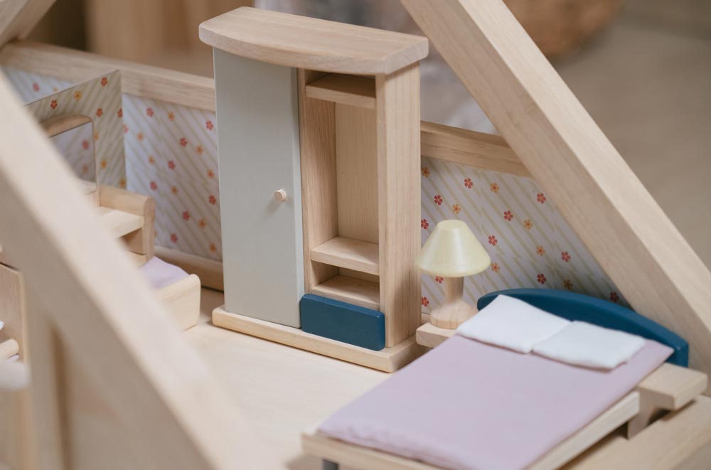 A close up of the wardrobe from the PlanToys Bedroom Dolls House Furniture set placed in a room in a wooden dolls house. 