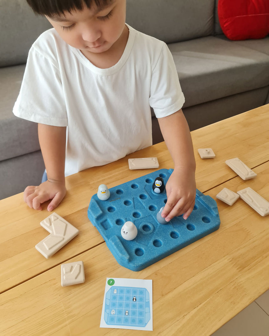 Close up of a boy picking up a penguin piece from the Plan Toys eco-friendly wooden finding penguin game on a wooden table