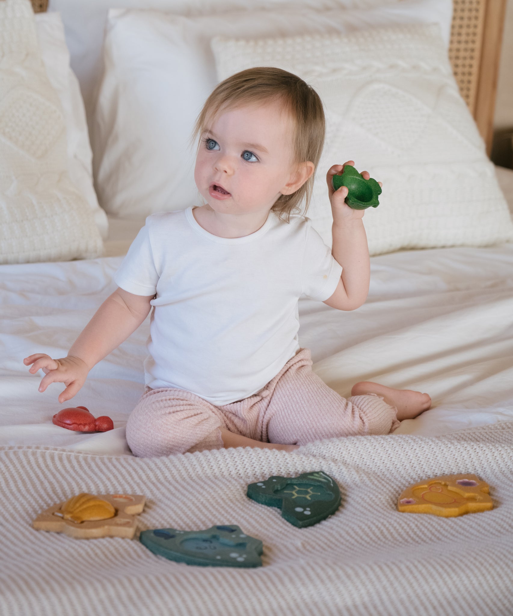 A child sitting on a bed playing with the PlanToys Marine Puzzle.