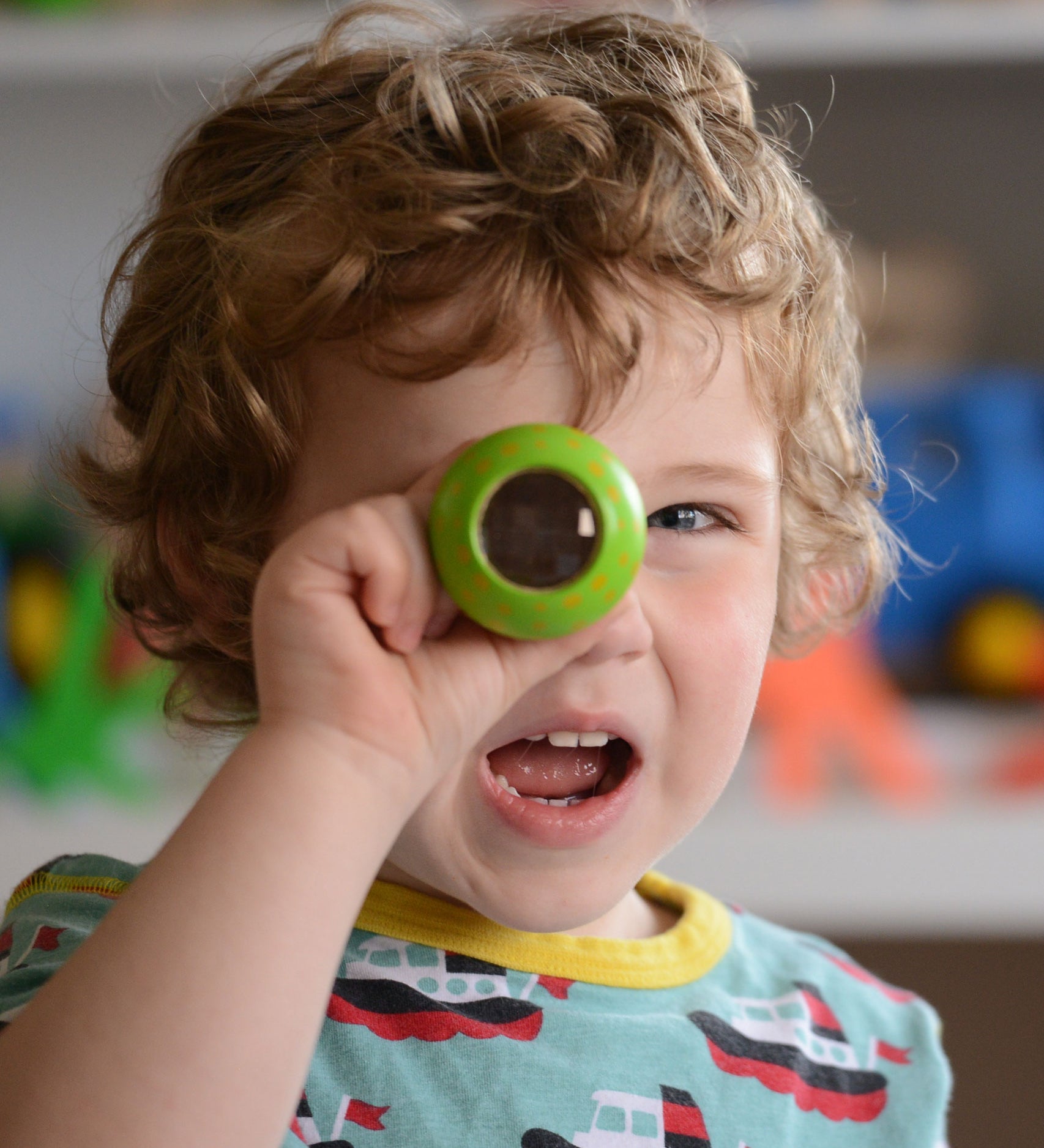 A child holding a green PlanToys Mushroom Kaleidoscope up to their eye. 