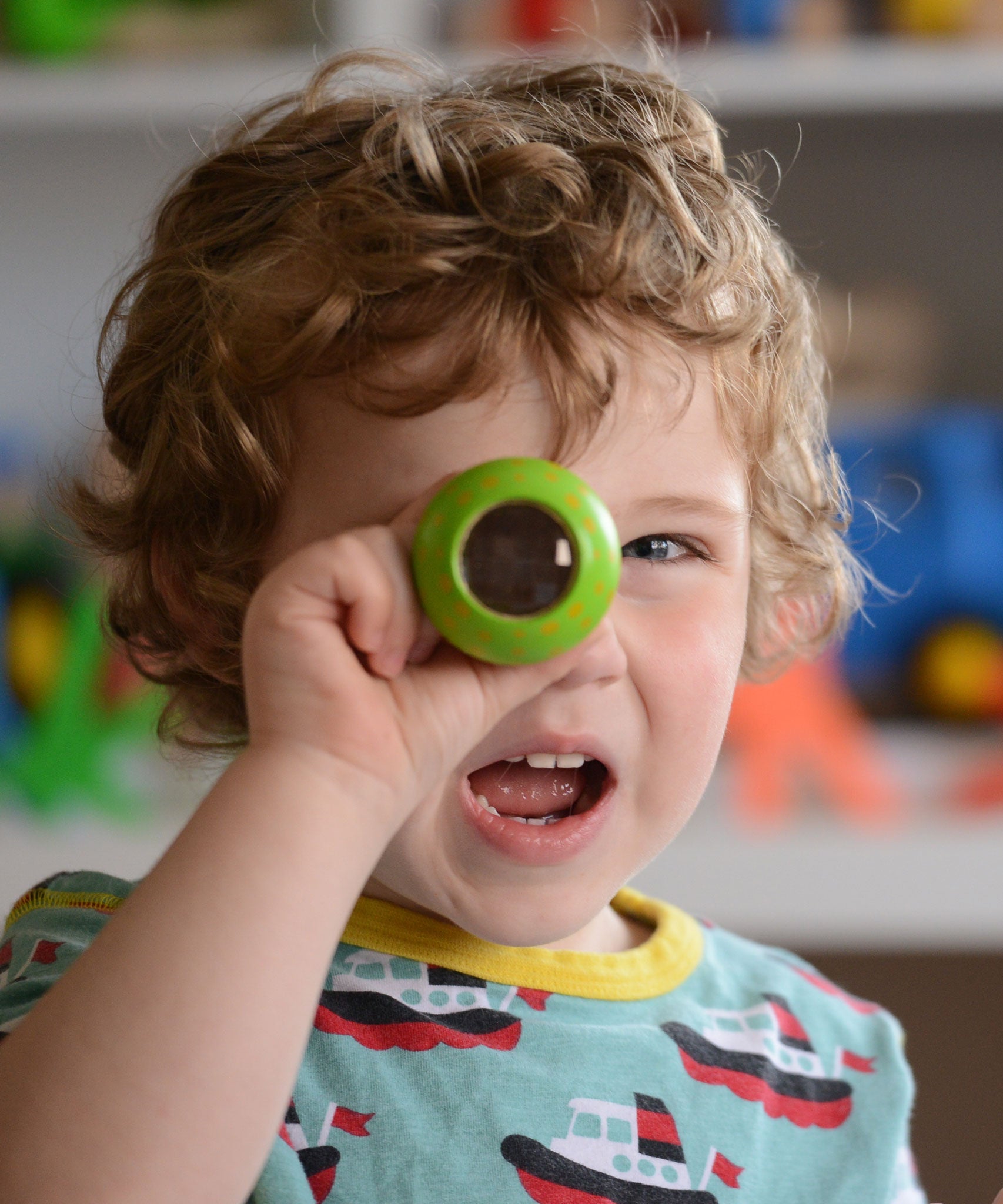 A child holding a green PlanToys Mushroom Kaleidoscope up to their eye. 