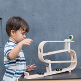 A child playing with the PlanToys Ramp Racer. The ramp racer has been placed on a PlanToys table. 