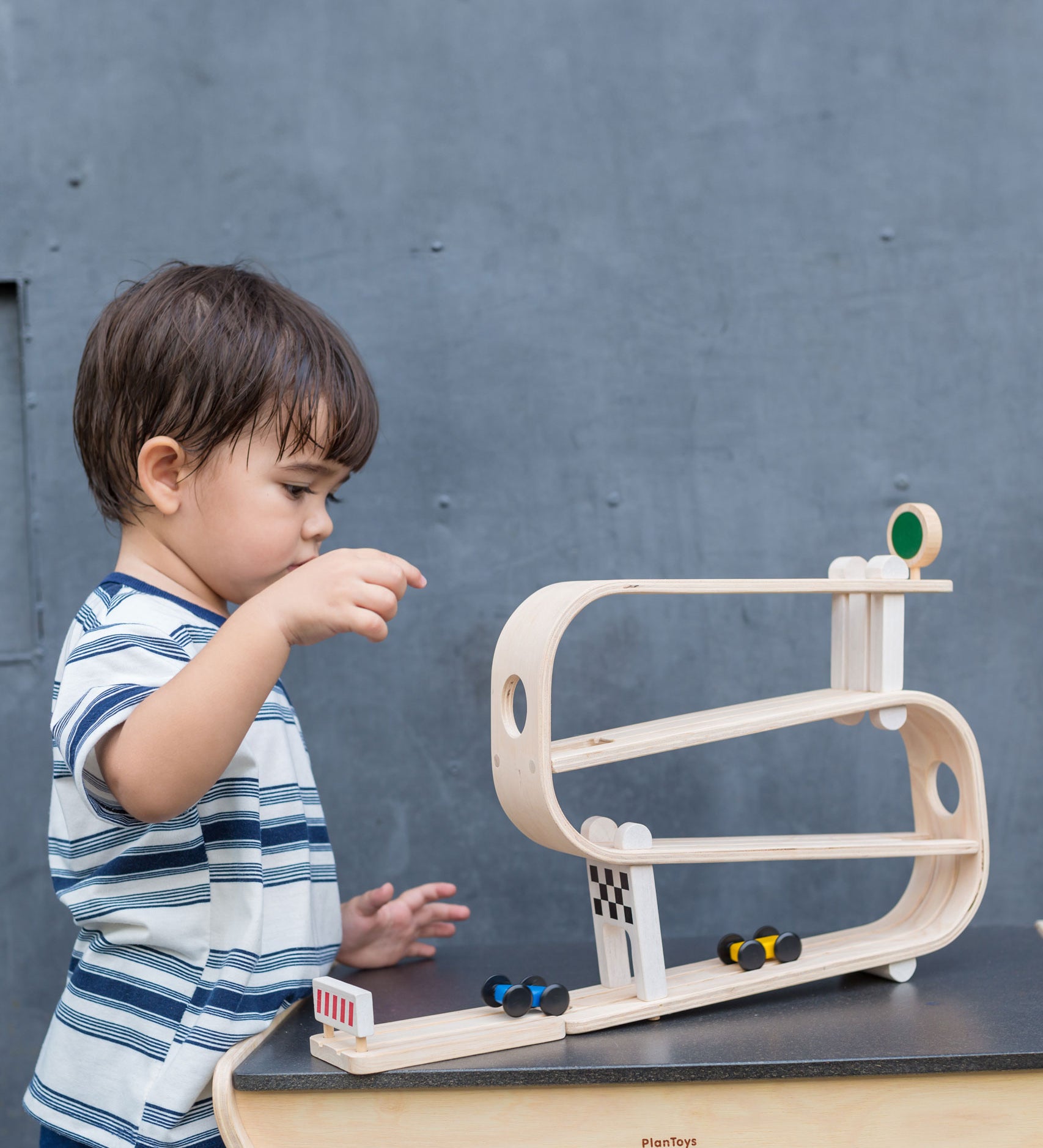 A child playing with the PlanToys Ramp Racer. The ramp racer has been placed on a PlanToys table. 