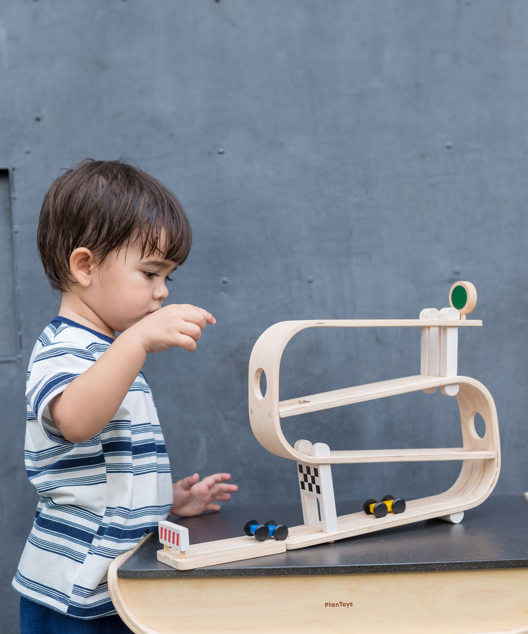 A child playing with the PlanToys Ramp Racer. The ramp racer has been placed on a PlanToys table. 