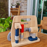 Plan Toys eco-friendly wooden carpenter role play tools set on a wooden table in front of a large window and green plant