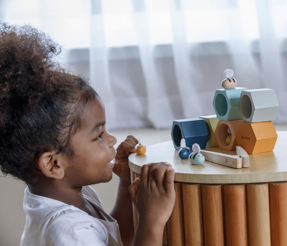 The PlanToys Bee Hives in the Orchard colour way placed side table. A child can be seen crouching in front of the table taking a close look at the bees.