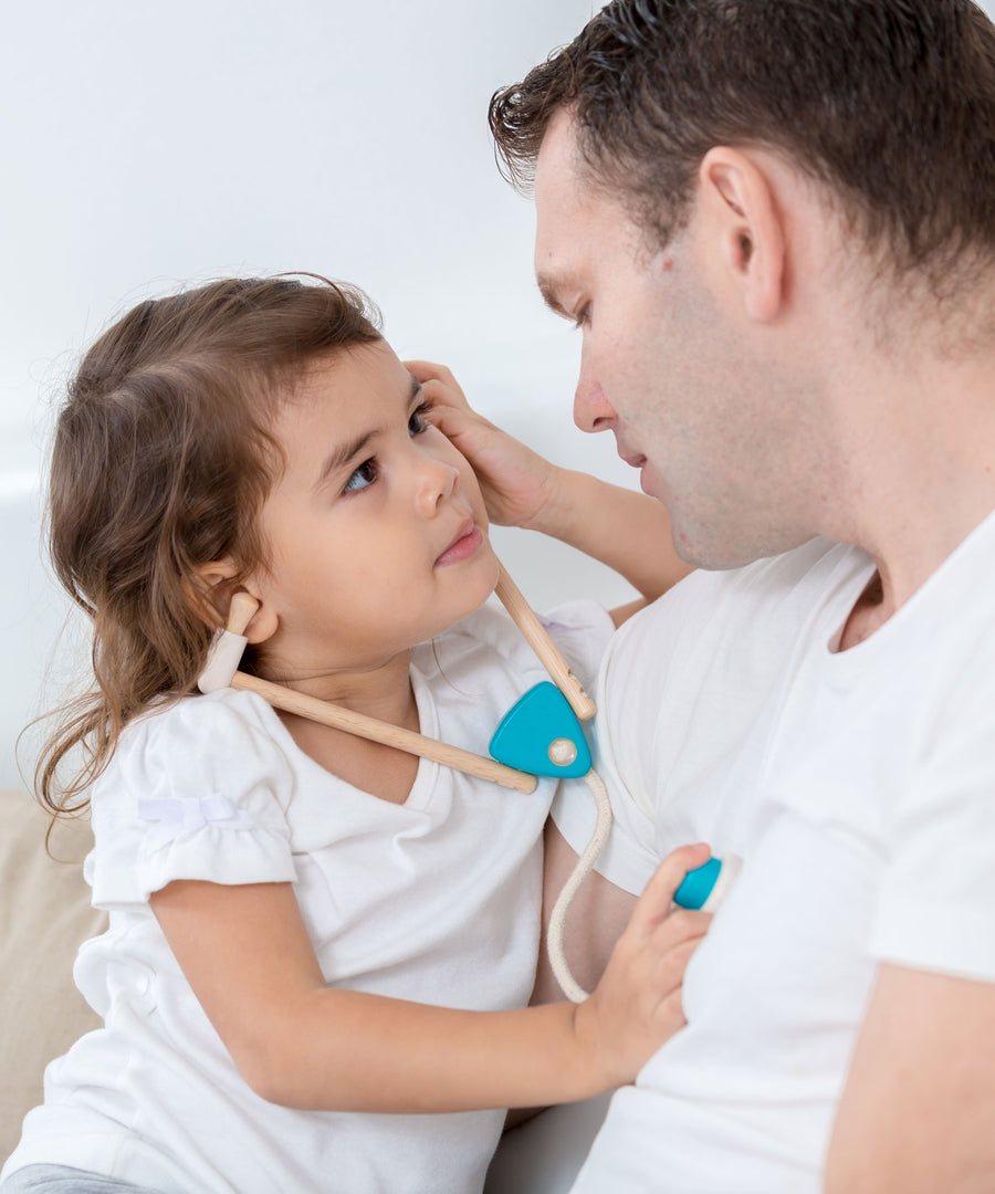 A child and adult playing with the PlanToys Doctor Set, the child has the stethoscope on and is listening to the adult's heart.