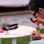 Child using the red lens from the PlanToys Detective Role Play Set to read the PlanToys newspaper