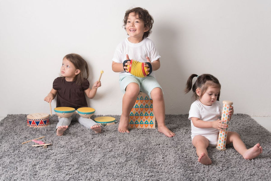 Three children playing Plan Toys musical instrument toys including a concertina