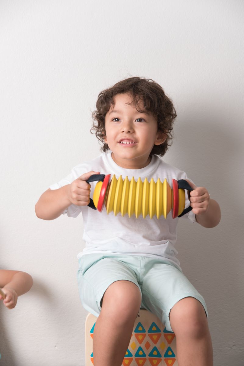 Child playing the Plan Toys Musical Concertina toy sat on a rhythm box.