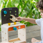 A child sitting on the ground playing with the PlanToys Workbench.