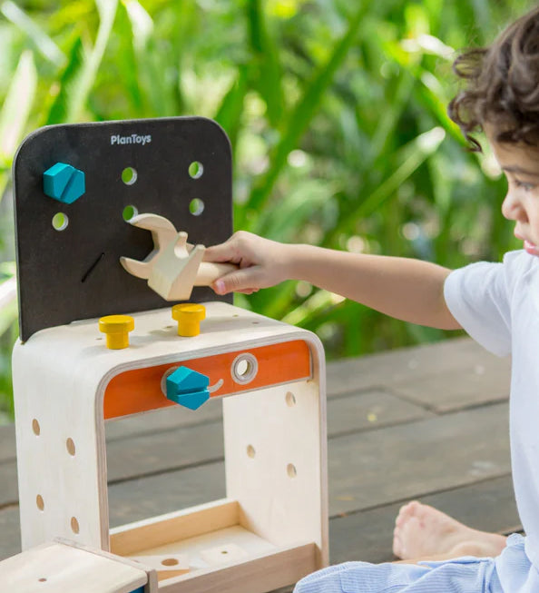 A child sitting on the ground playing with the PlanToys Workbench.