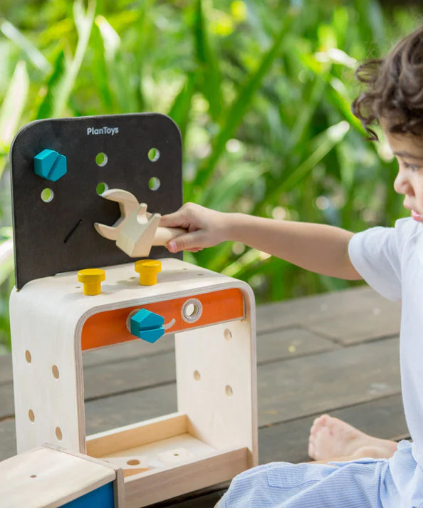 A child sitting on the ground playing with the PlanToys Workbench.