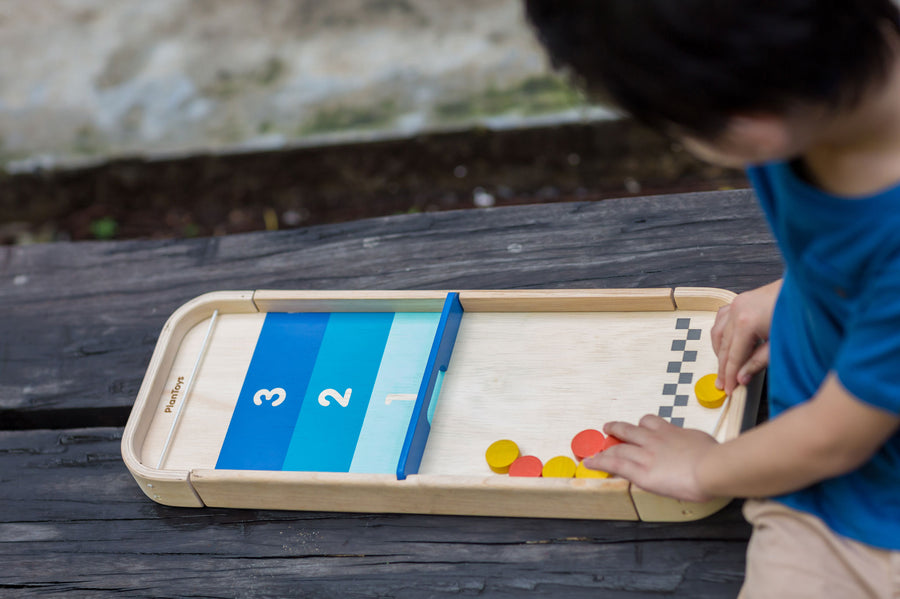 A child playing with the PlanToys 2-In-1 Shuffleboard Game on a plain background. 