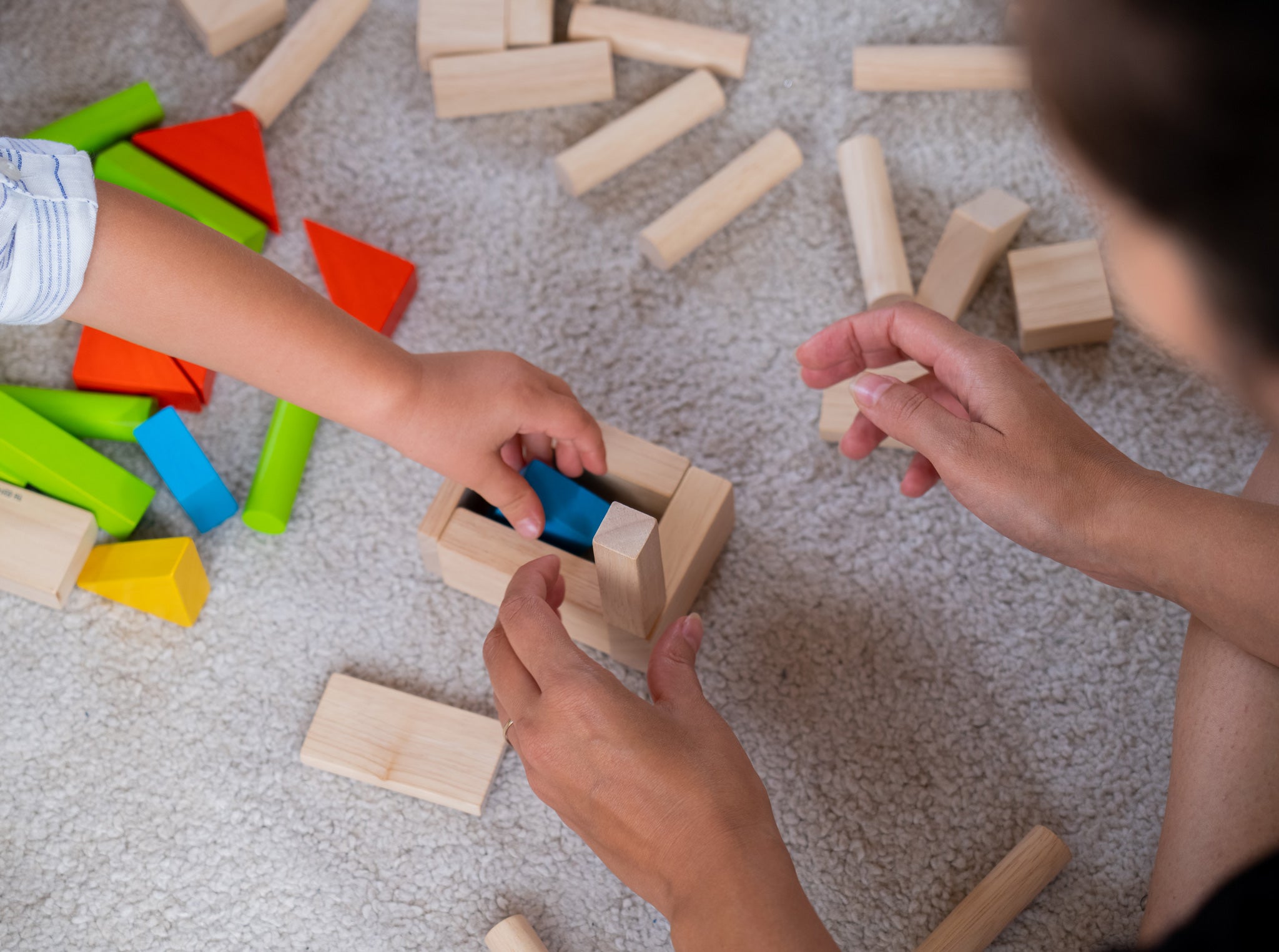 A close up of a child's and adult's hands playing with the PlanToys 40 unit Colourful Block set. 