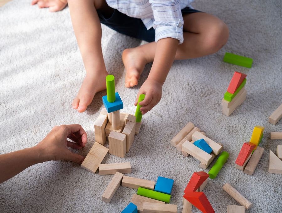 A close up of a child's hand playing with the PlanToys 40 unit Colourful Block set. 