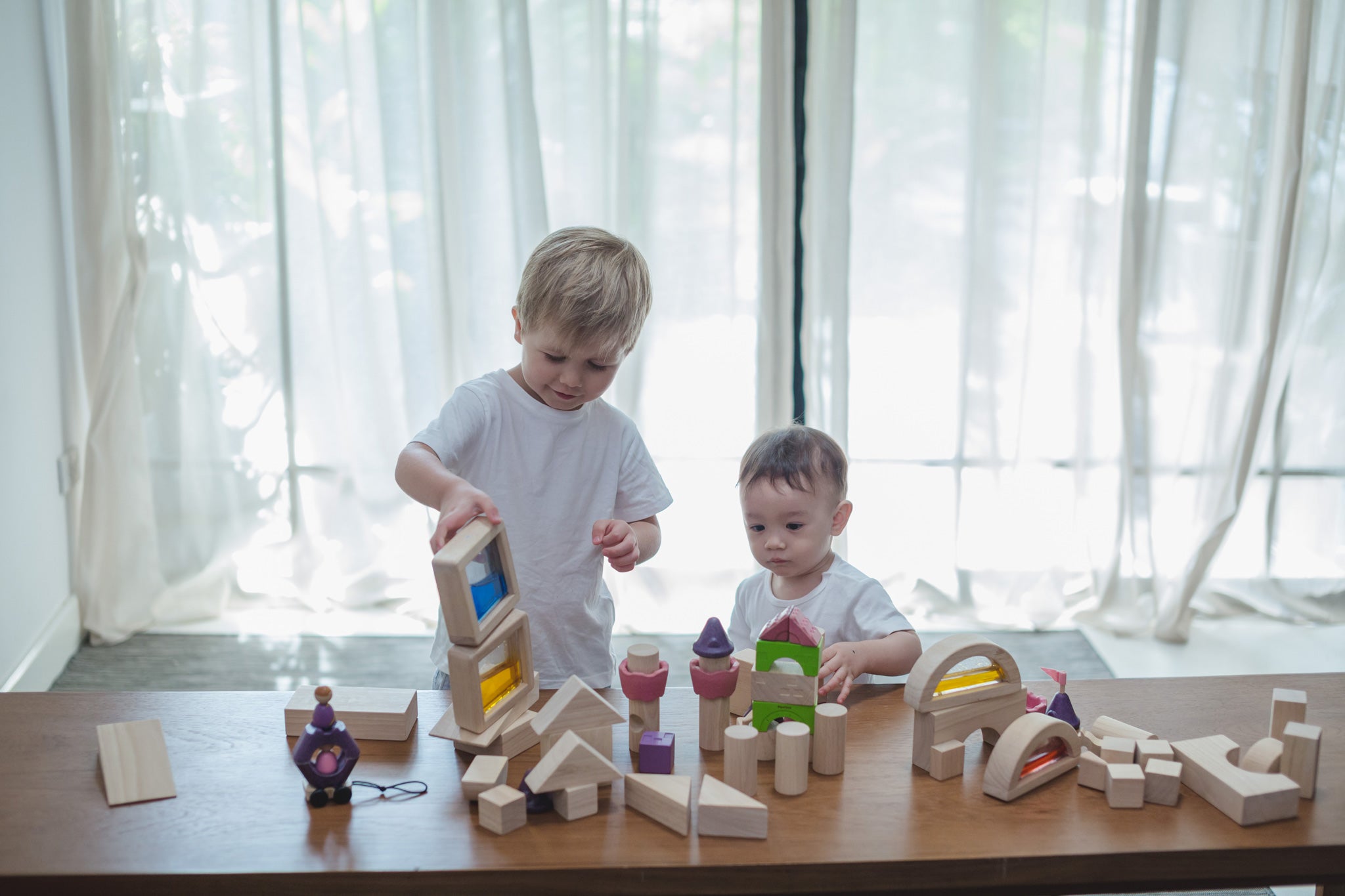 Two children playing with a collection of different PlanToys block sets. They have the PlanToys natural wooden 50 Unit Building Block set along with the castle blocks and water window blocks.