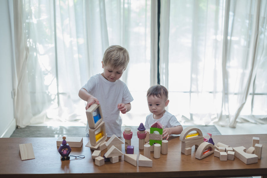 Two children playing with a collection of different PlanToys block sets. They have the PlanToys natural wooden 50 Unit Building Block set along with the castle blocks and water window blocks.