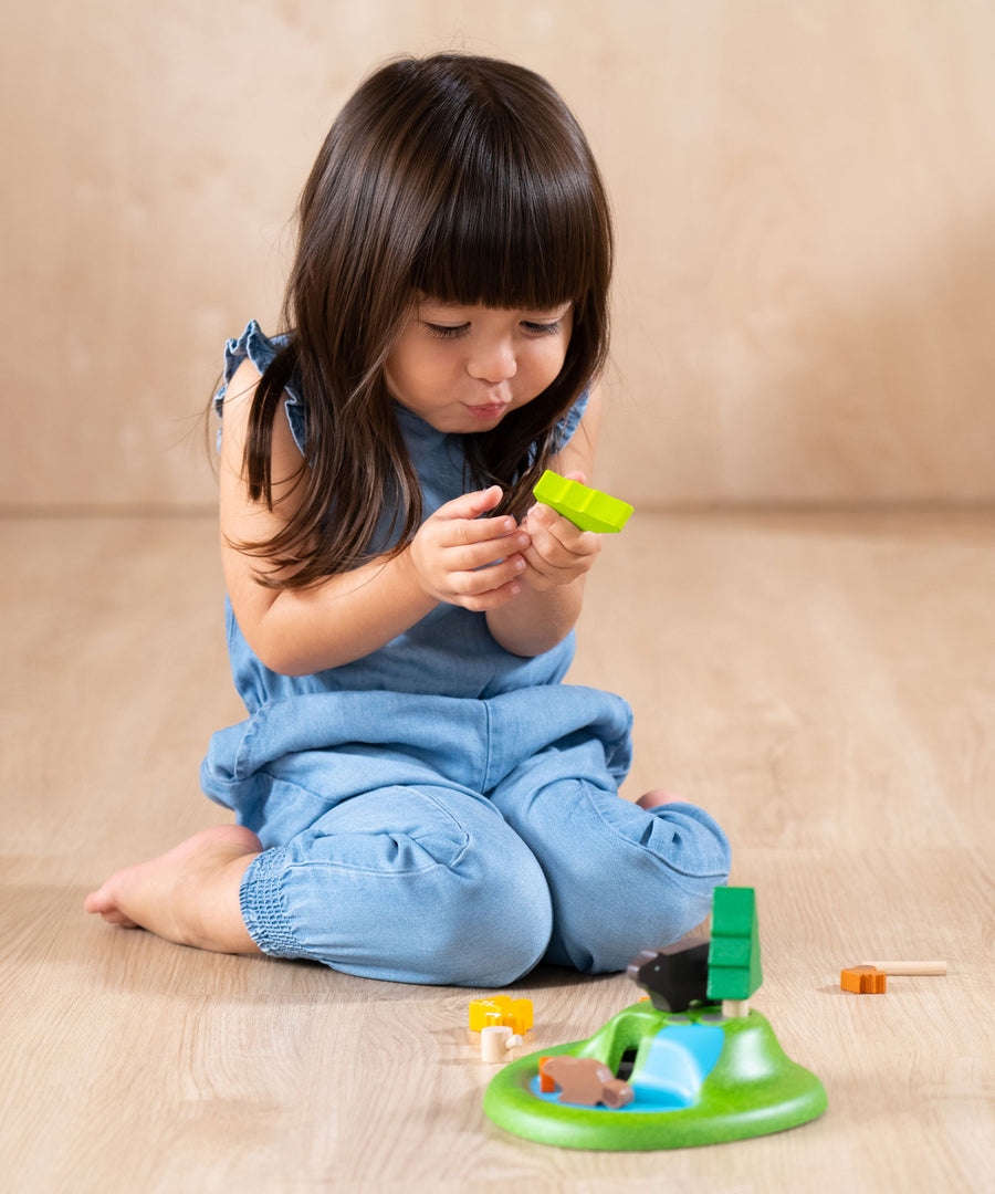 A child playing with the PlanToys Animal Set on a wooden floor. 