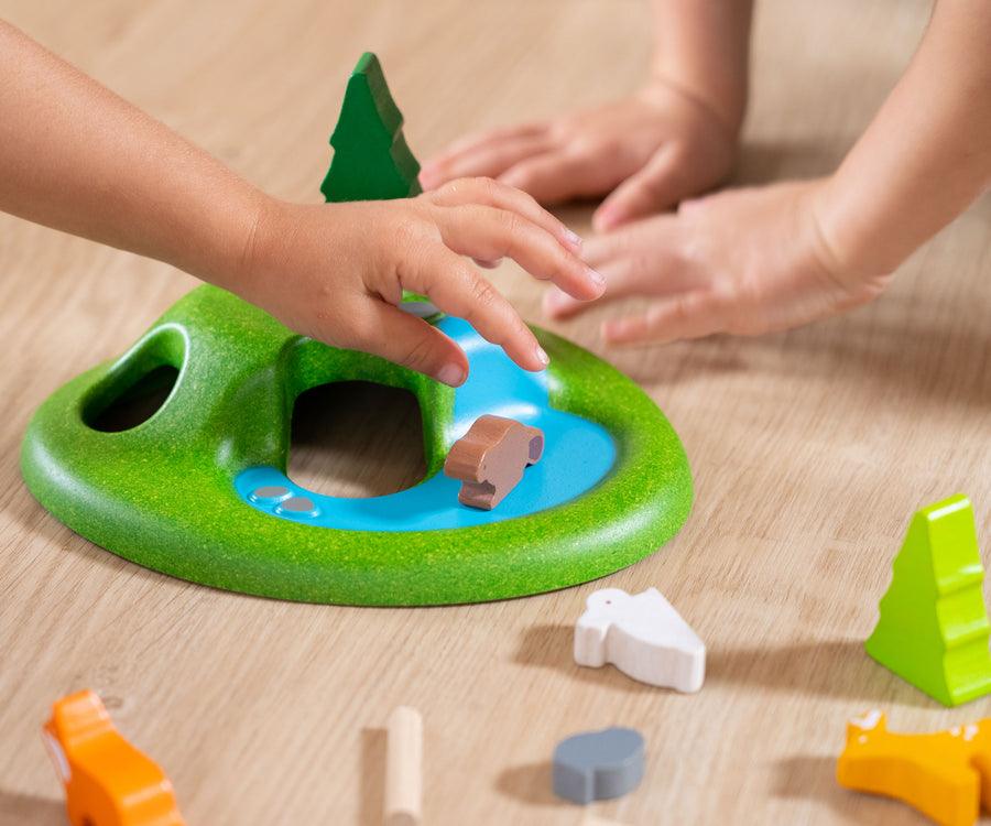 A close up of children's hands playing with the PlanToys Animal Set on a wooden floor. 