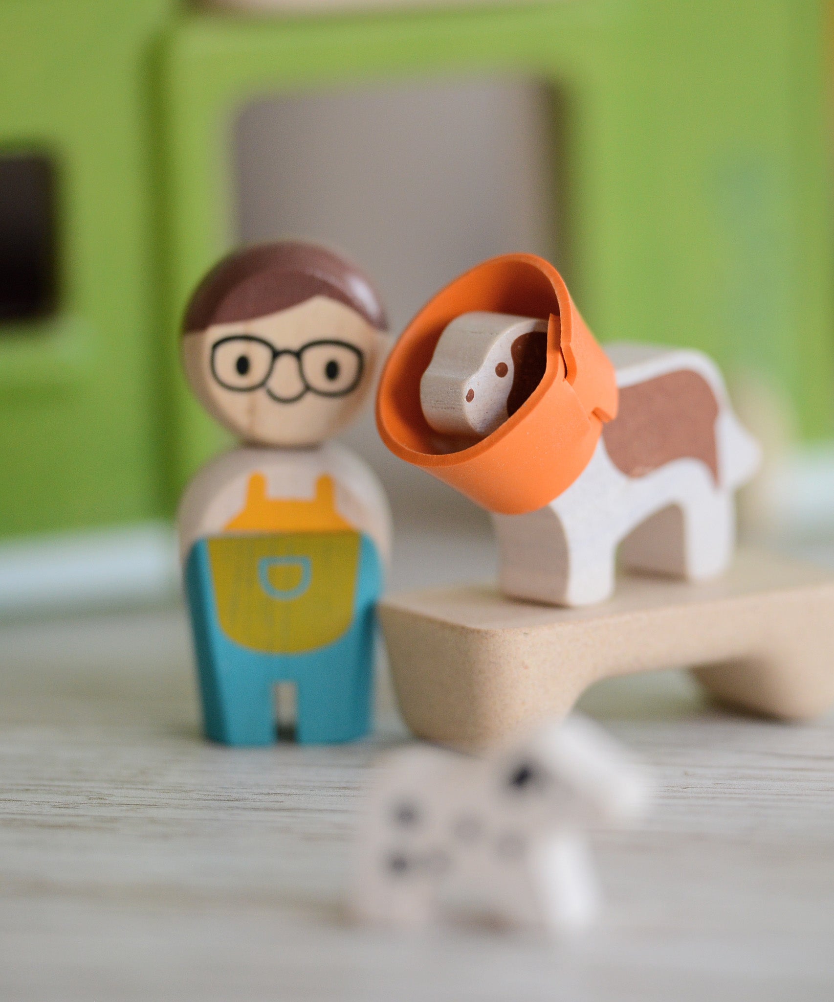 A closeup of the PlanToys wooden dog from the pet shop, with a rubber cone around its neck.