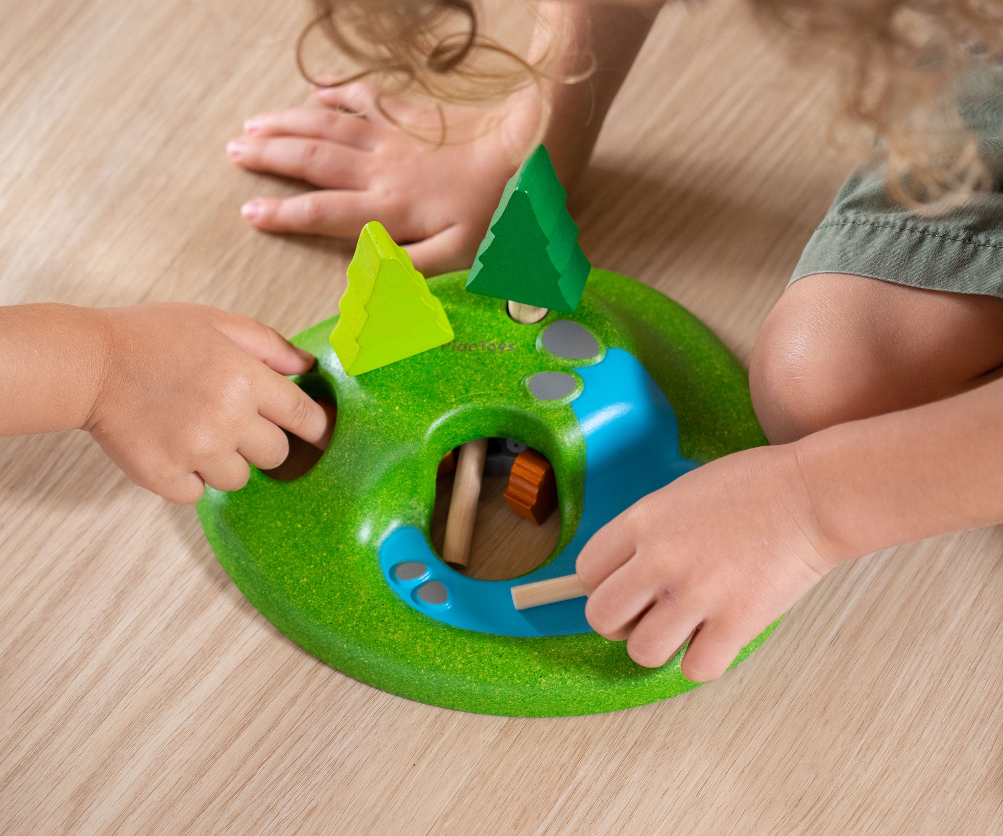 A close up of children's hands playing with the PlanToys Animal Set on a wooden floor. 