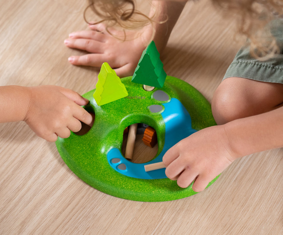 A close up of children's hands playing with the PlanToys Animal Set on a wooden floor. 