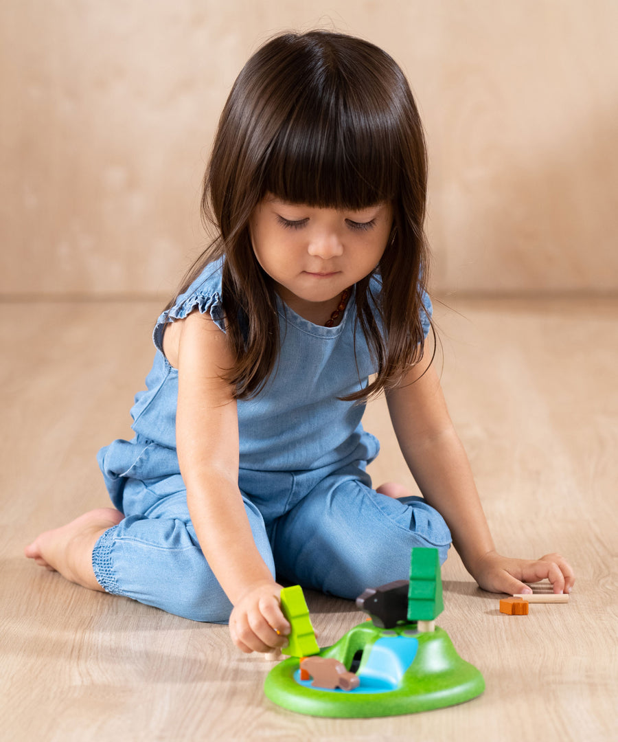 A child playing with the The PlanToys Animal Set on a wooden floor. 