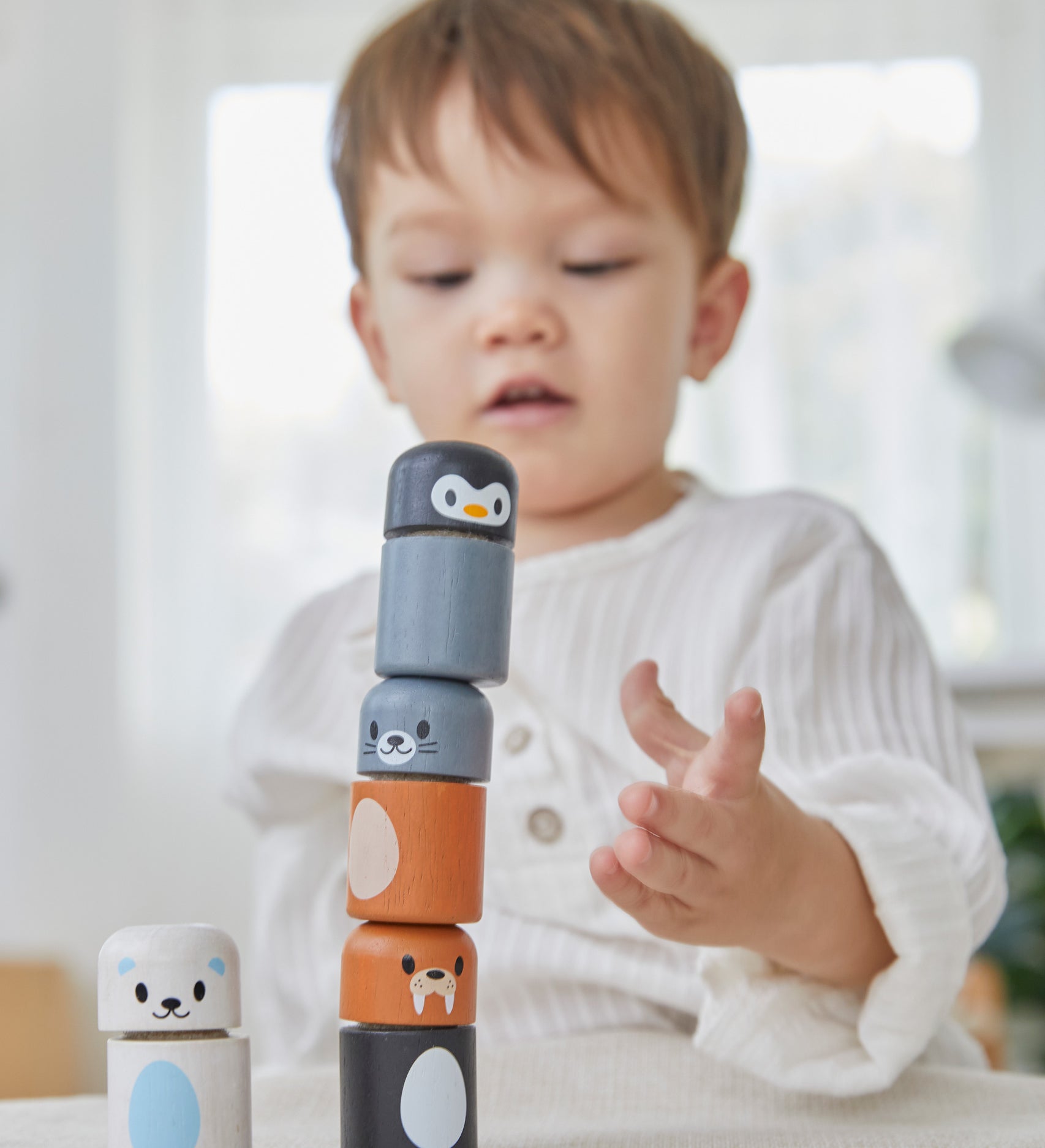 A child making a tower with the PlanToys arctic animals matching figures on a white table