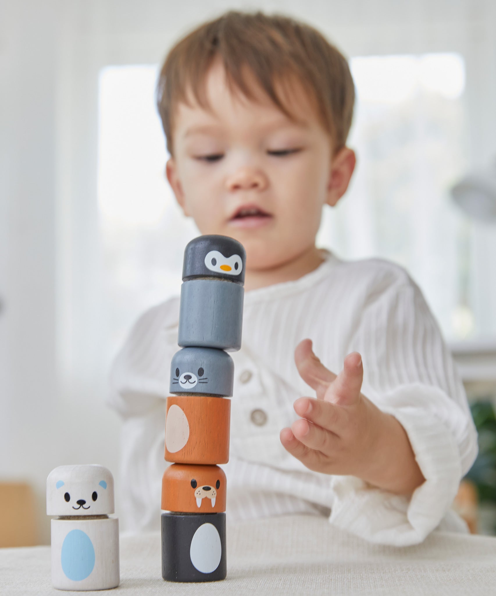 A child making a tower with the PlanToys arctic animals matching figures on a white table