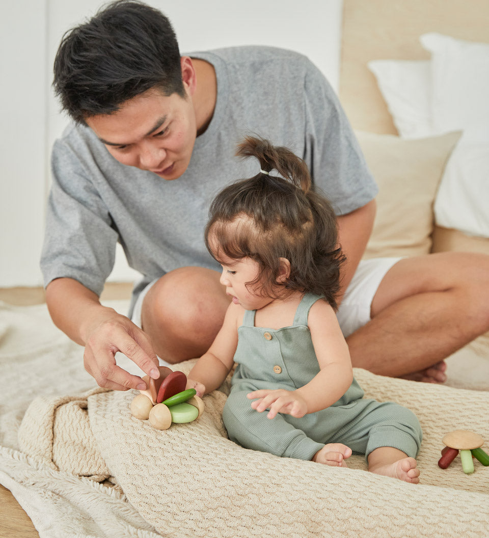 Young girl and man sat on a blanket playing with the PlanToys wooden baby car toy