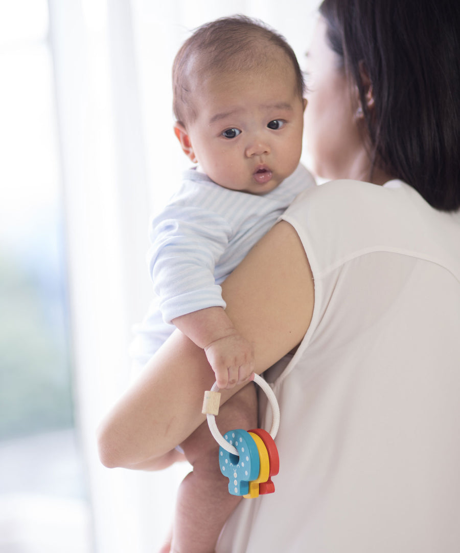 A baby being held by and adult, the baby is holding on to the PlanToys Baby Key Rattle. 