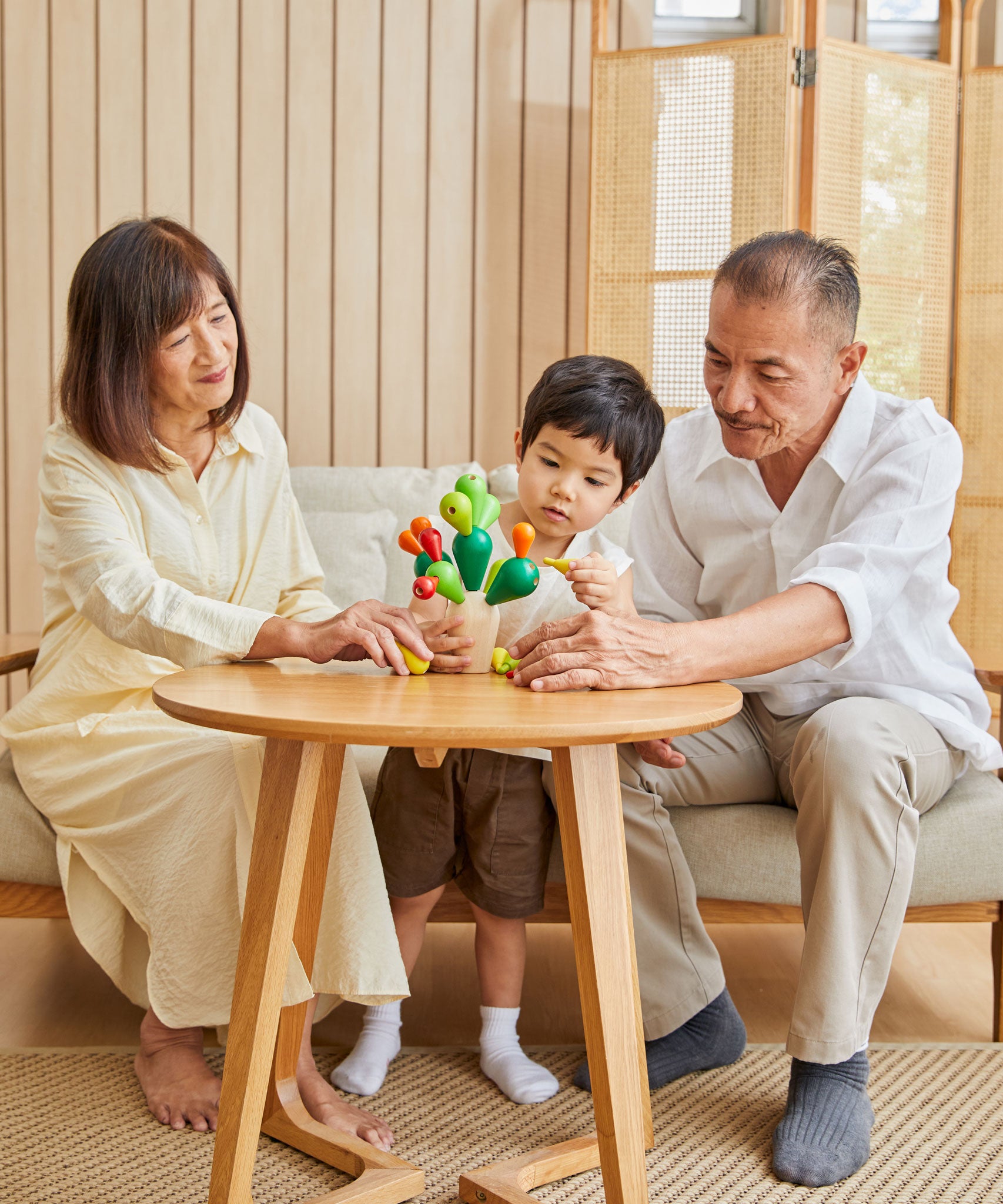 A family of two adults and a child playing with the PlanToys Balancing Cactus. 