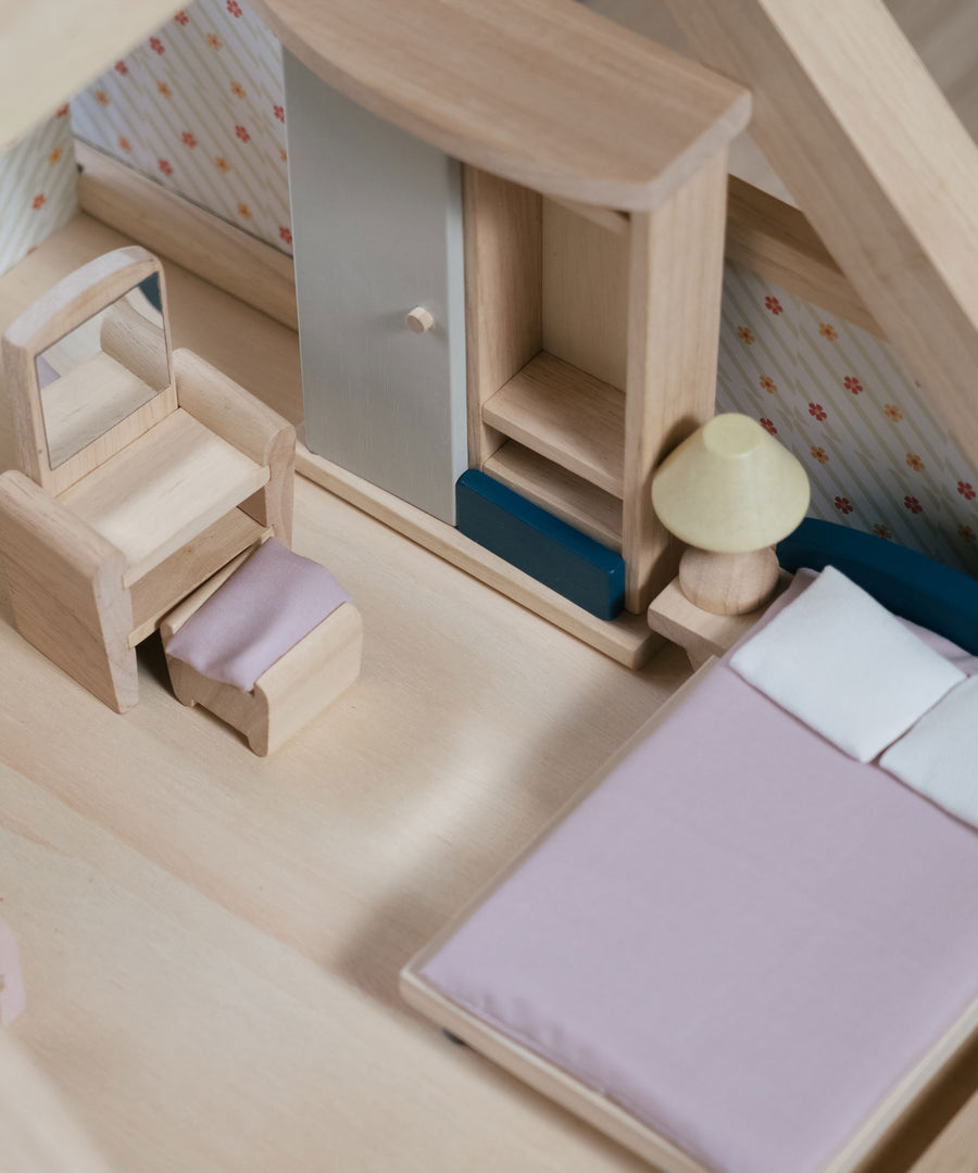 A close up of the PlanToys Bedroom Dolls House Furniture set in a wooden dolls house. 
