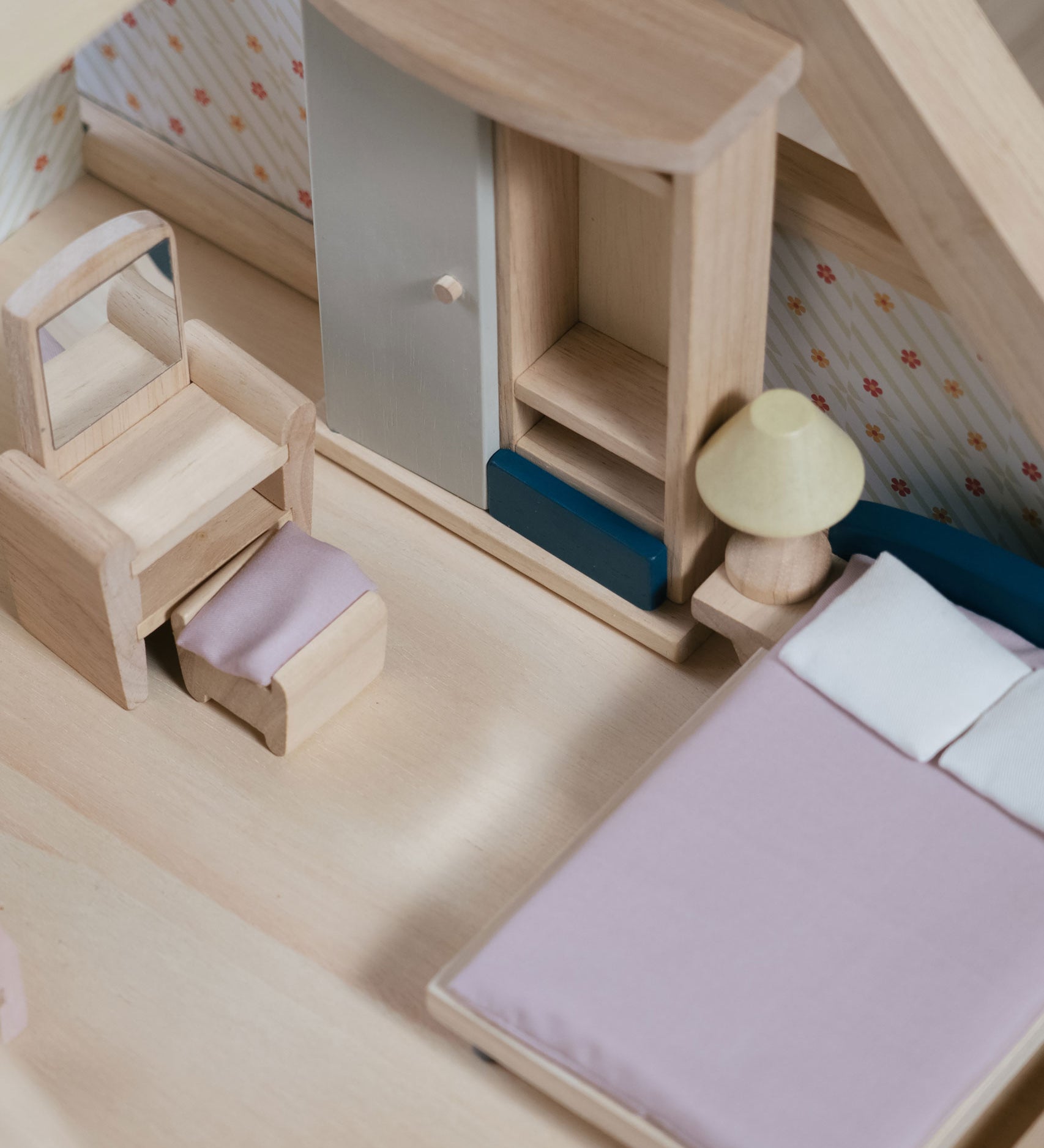 A close up of the PlanToys Bedroom Dolls House Furniture set in a wooden dolls house. 
