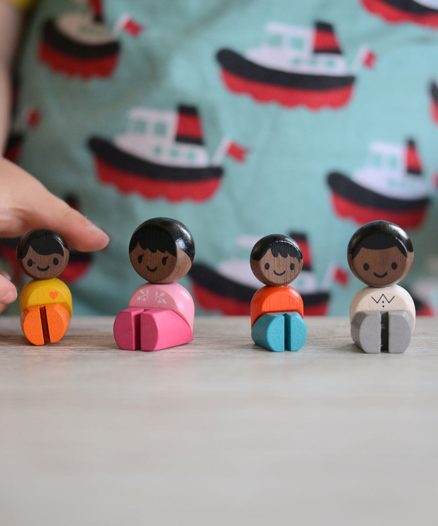 The PlanToys PlanWorld Black Skin, Black Hair Family sitting down, a child's hand can be seen reaching for one of them. 