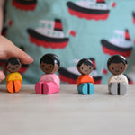 The PlanToys PlanWorld Black Skin, Black Hair Family sitting down, a child's hand can be seen reaching for one of them. 