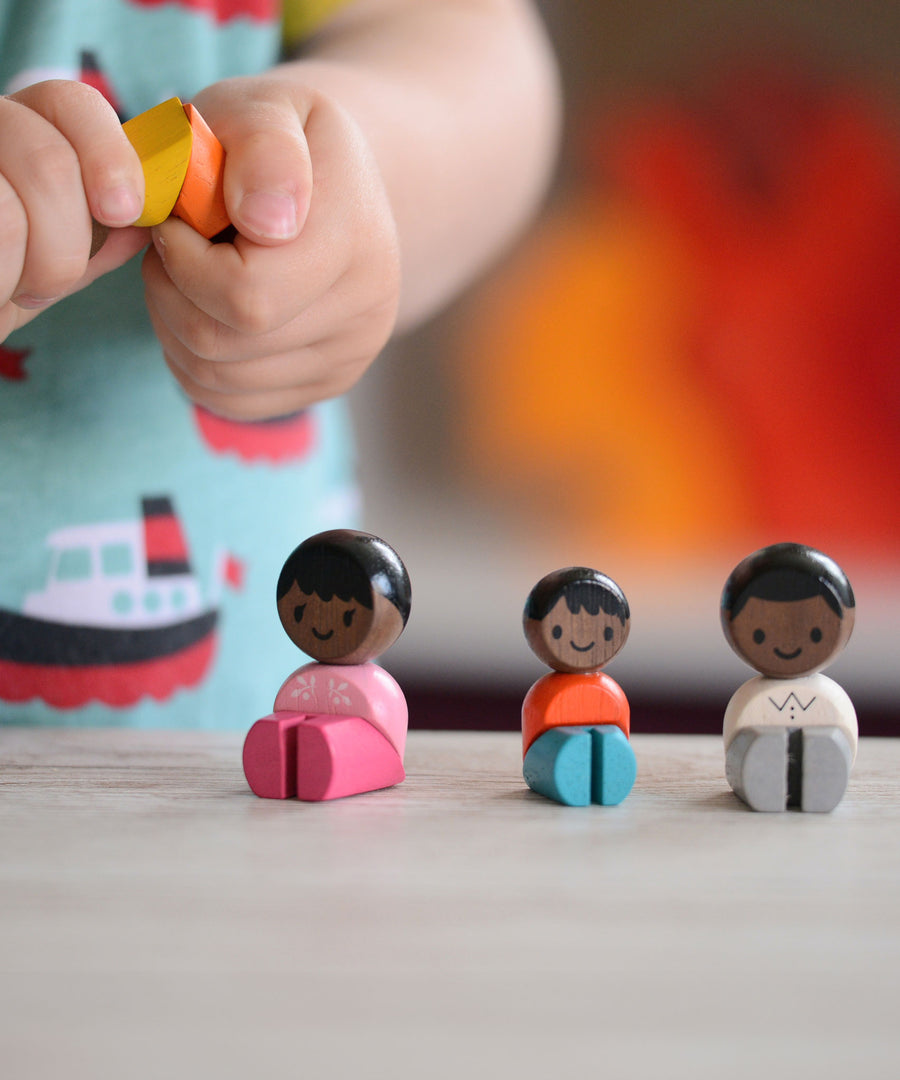 The PlanToys PlanWorld Black Skin, Black Hair Family sitting down, a child is holding one of them. 