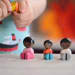 The PlanToys PlanWorld Black Skin, Black Hair Family sitting down, a child is holding one of them. 