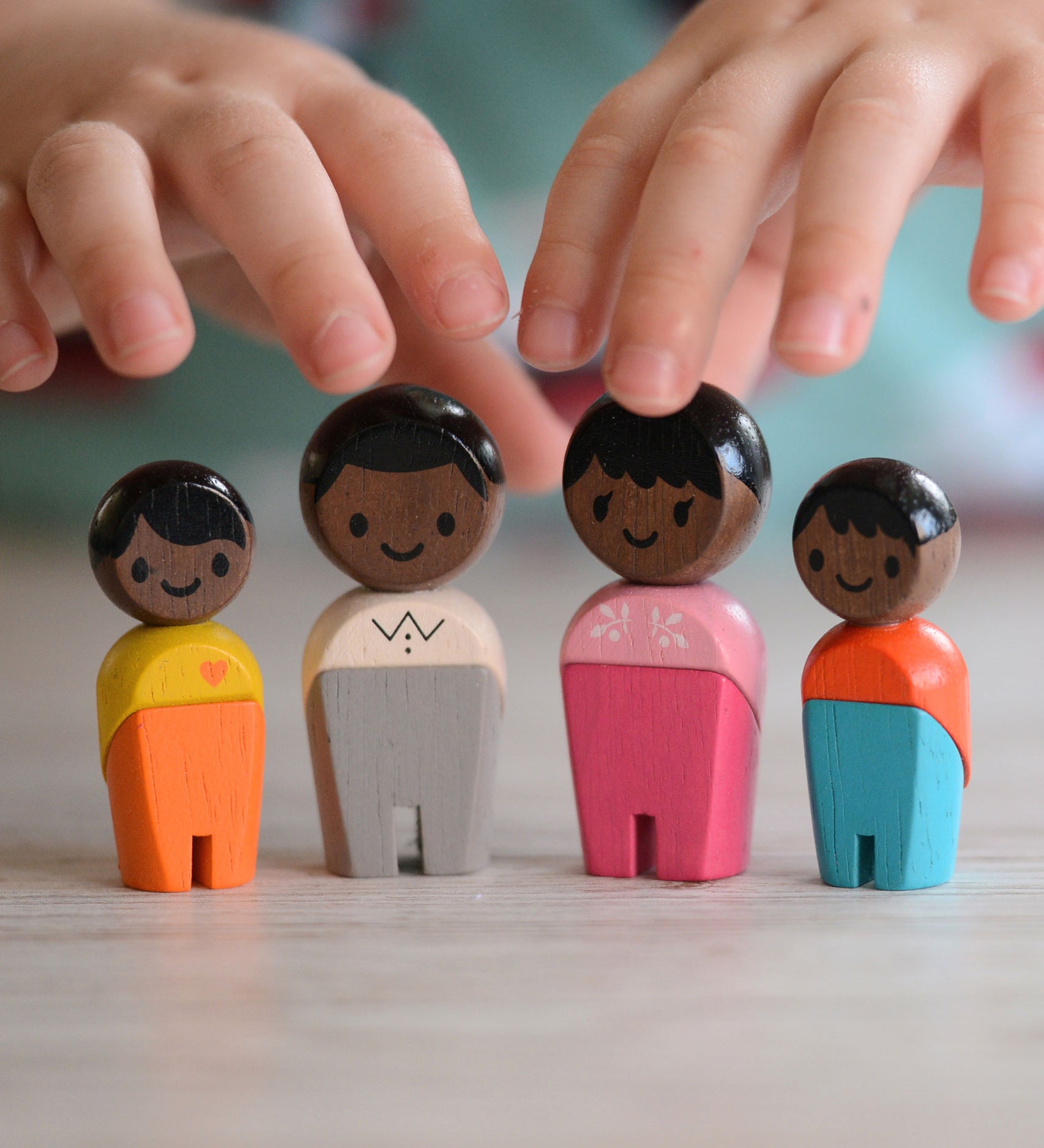 The PlanToys PlanWorld Black Skin, Black Hair Family stood up, a child's hand can be seen reaching for them. 