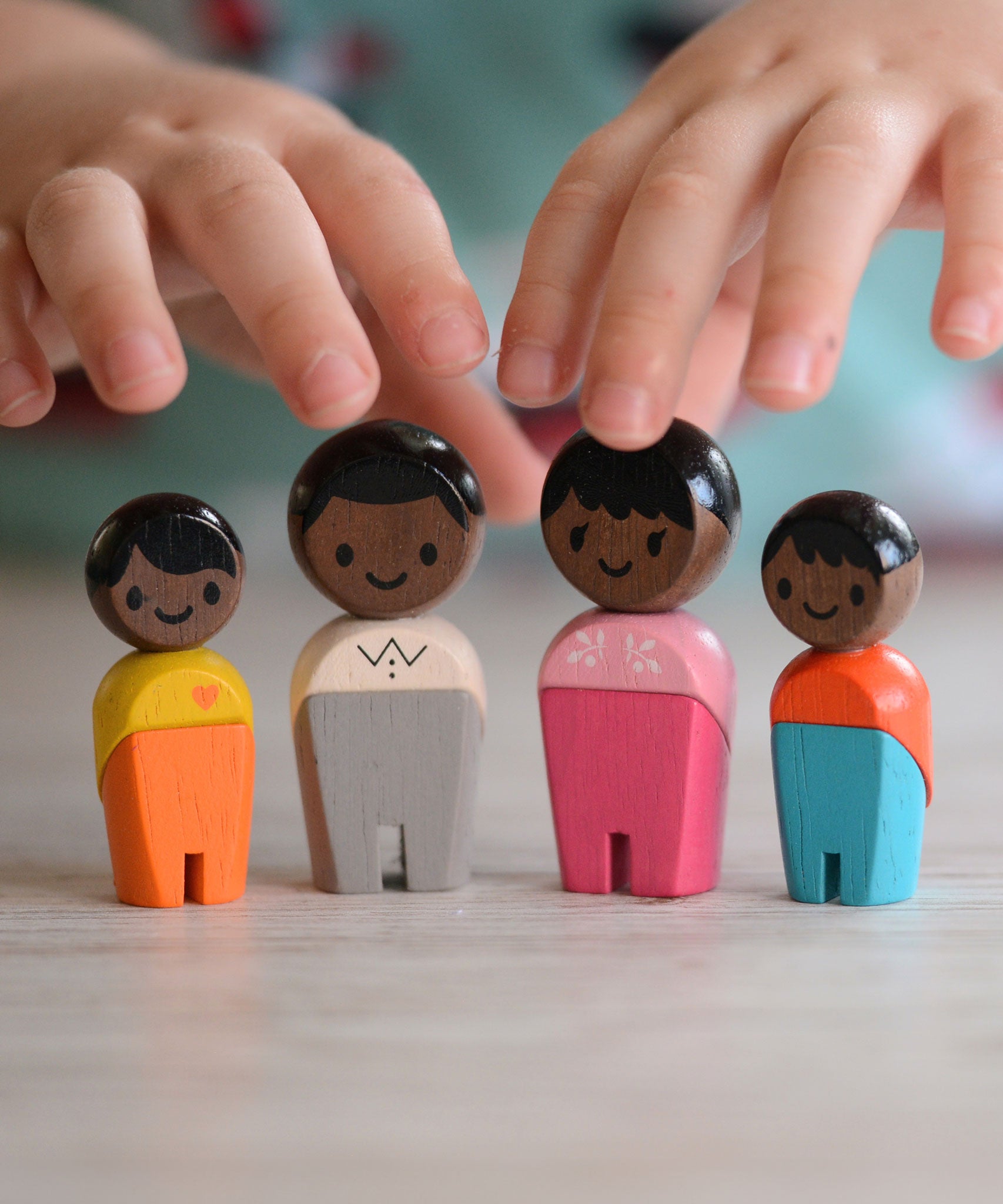 The PlanToys PlanWorld Black Skin, Black Hair Family stood up, a child's hand can be seen reaching for them. 