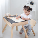 A child sitting by a PlanToys Black Table & Chair. The child is writing and a piece of paper. 