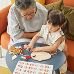 Young girl and woman sat at a round table playing with the PlanToys wooden build a face toy