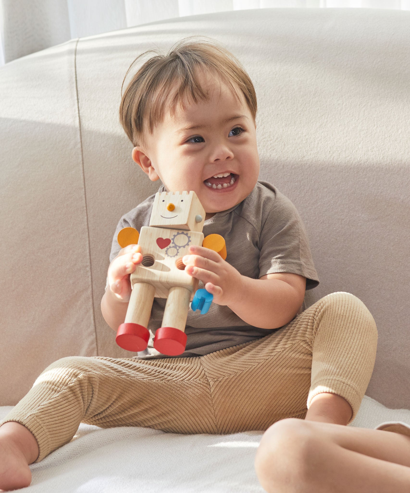 A child holding on to a Plan Toys Build a Robot toy with a smile on both their faces. 