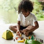 A child sitting on a floor playing with the PlanToys PlanWorld Camping Set.
