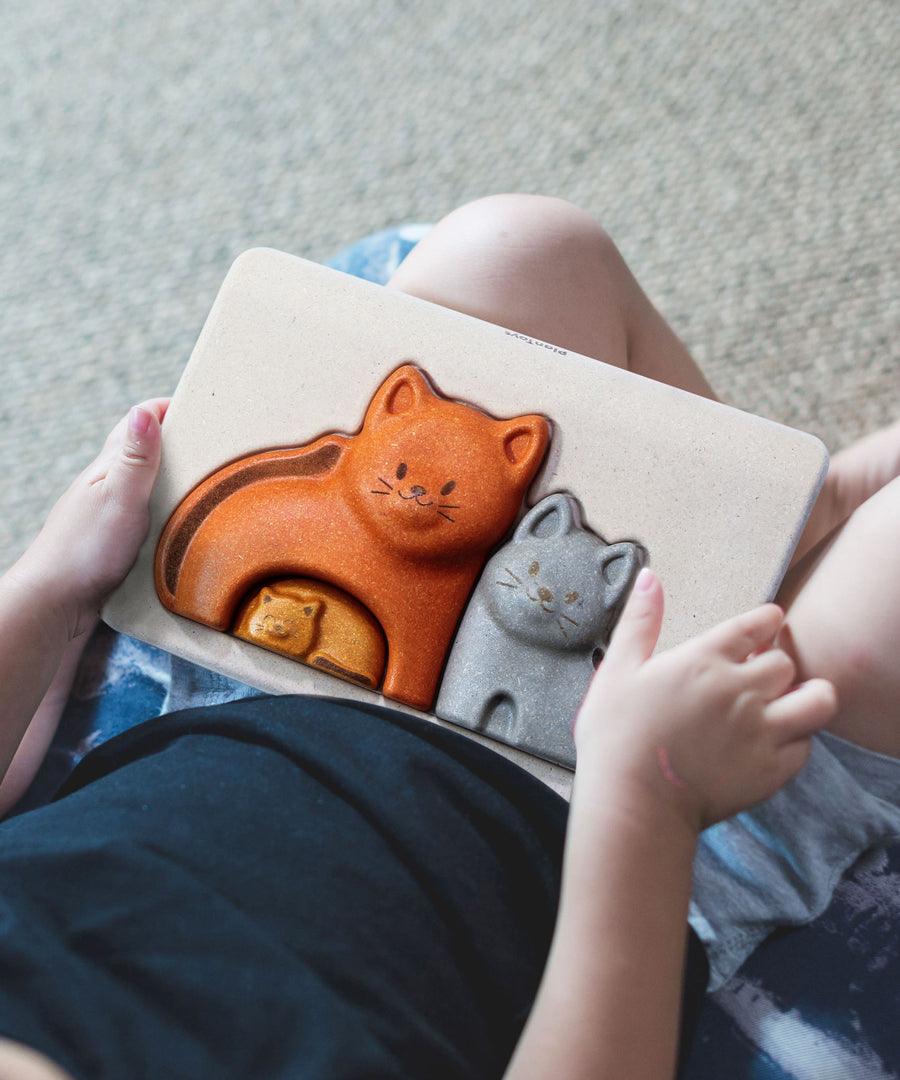 A close up of a child's hands holding the PlanToys Cat Puzzle.