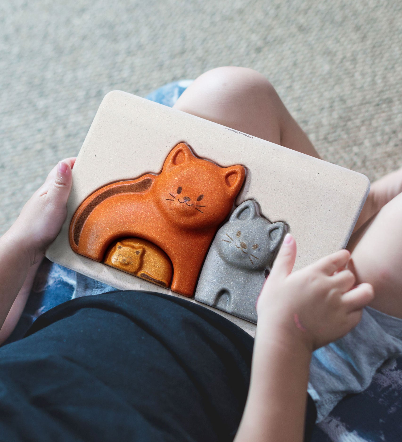 A close up of a child's hands holding the PlanToys Cat Puzzle.