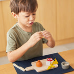 Close up of a young boy holding pieces of play food from the PlanToys charcuterie board toy set